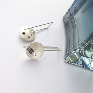 Custom-made Silver CZ Circle Drop Earrings are placed on the white surface near the blue perfume bottle..