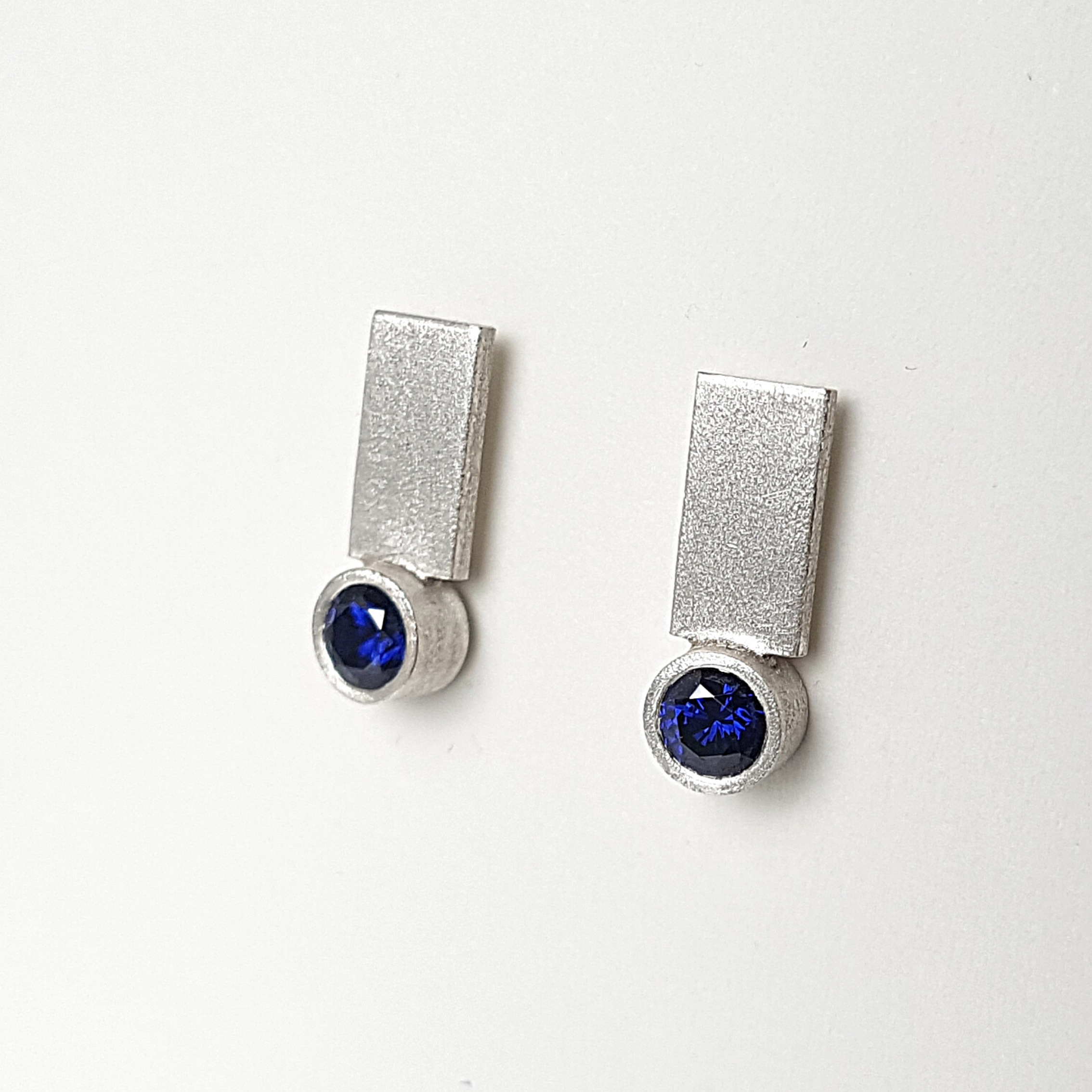 Sterling silver earrings with dark blue cubic zirconia are hanging on a white stand.