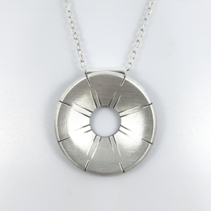 Contemporary silver pendant with rays is handing on the white holder.