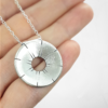 Silver circle pendant is displayed on the palm.