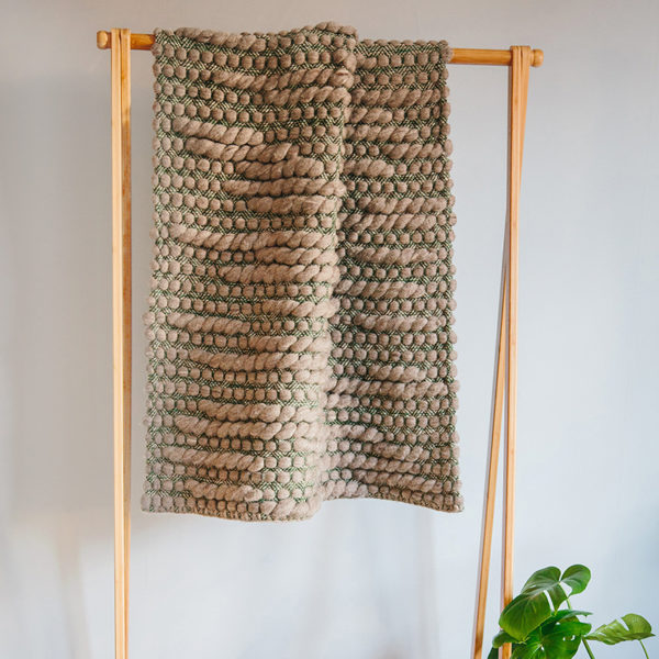 Handwoven 'Caterpillar' throw featuring Merino wool by Cassandra Sabo draped over a hanging rail