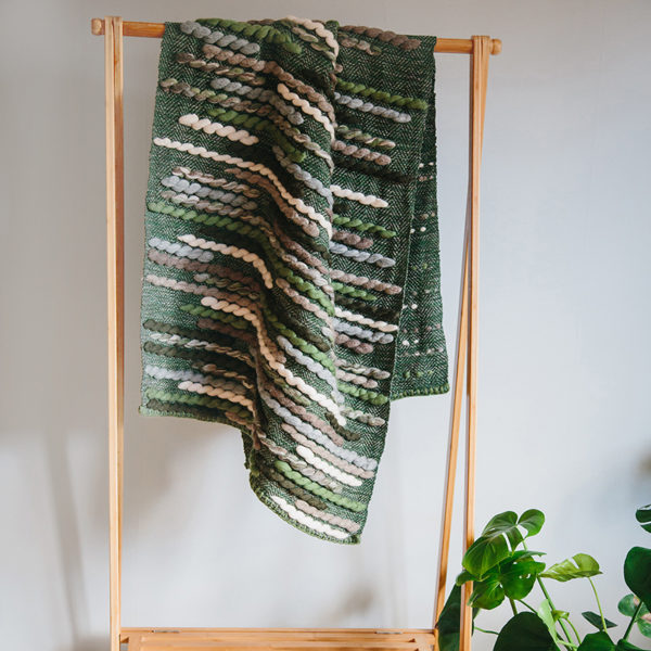 Handwoven 'Caterpillar' throw featuring Merino wool by Cassandra Sabo draped over a hanging rail