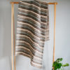 Handwoven 'Tendril' throw featuring Merino wool by Cassandra Sabo draped over a hanging rail