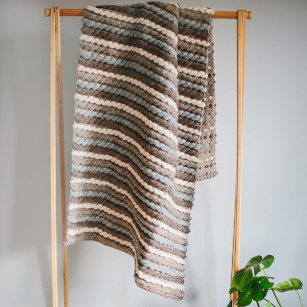Handwoven 'Tendril' throw featuring Merino wool by Cassandra Sabo draped over a hanging rail