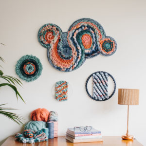 Cassandra Sabo’s ‘West Coast 8’ woven circular textile wall-hanging from her West Coast Collection hung on the wall with multiple artworks