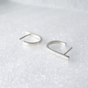 Statement minimalist J-shaped silver earrings are placed on the white surface.