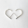 Minimalist J-shaped silver earrings are placed on the white surface.