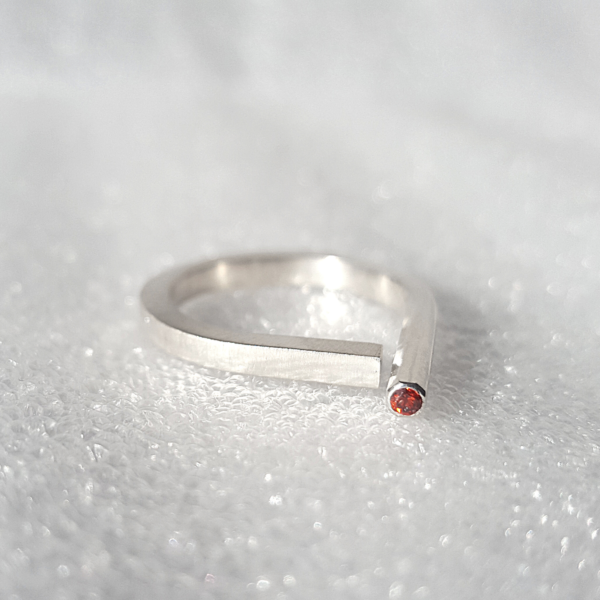 Sterling silver contemporary open ring with red garnet is placed on the white surface.