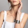 model touching her face with left arm wearing a wide cuff and a square silver pendant