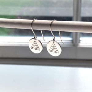 small circle earring with a triangle design dangling in front of a white window