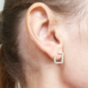 Square silver wire earrings on an earlobe.