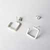 Handmade square silver wire earrings on a white table.