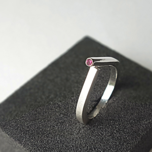 Geometric ring in sterling silver with crimson garnet stands on the black sponge.
