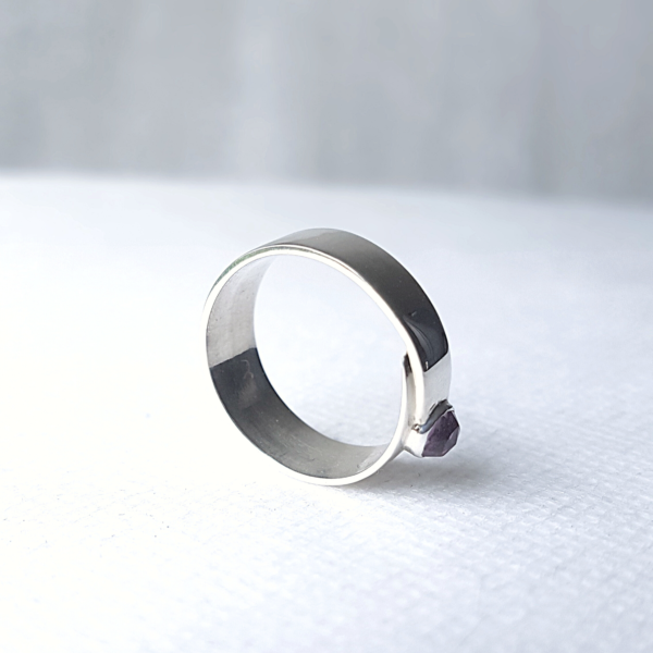 Overlap minimalist silver ring with amethyst stands on the white surface.