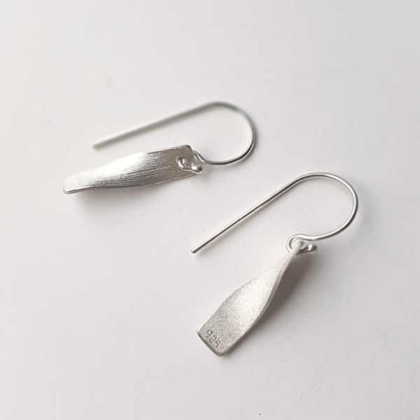 Handmade silver twisted dangle earrings on a white surface.