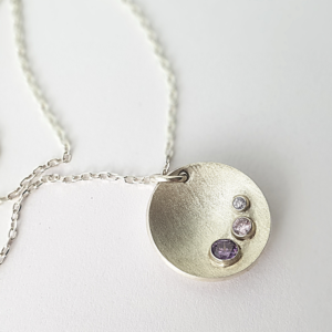 Handmade silver three stone pendant necklace on a white surface.