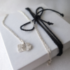 Personalised silver blossom and initial letter pendant necklace on a white gift box tied with black cotton string.