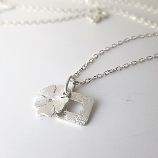 Unique initial and flower pendant necklace on a white surface.