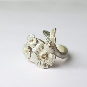 Unique handmade flower and butterfly ring in silver and gold on a white surface.
