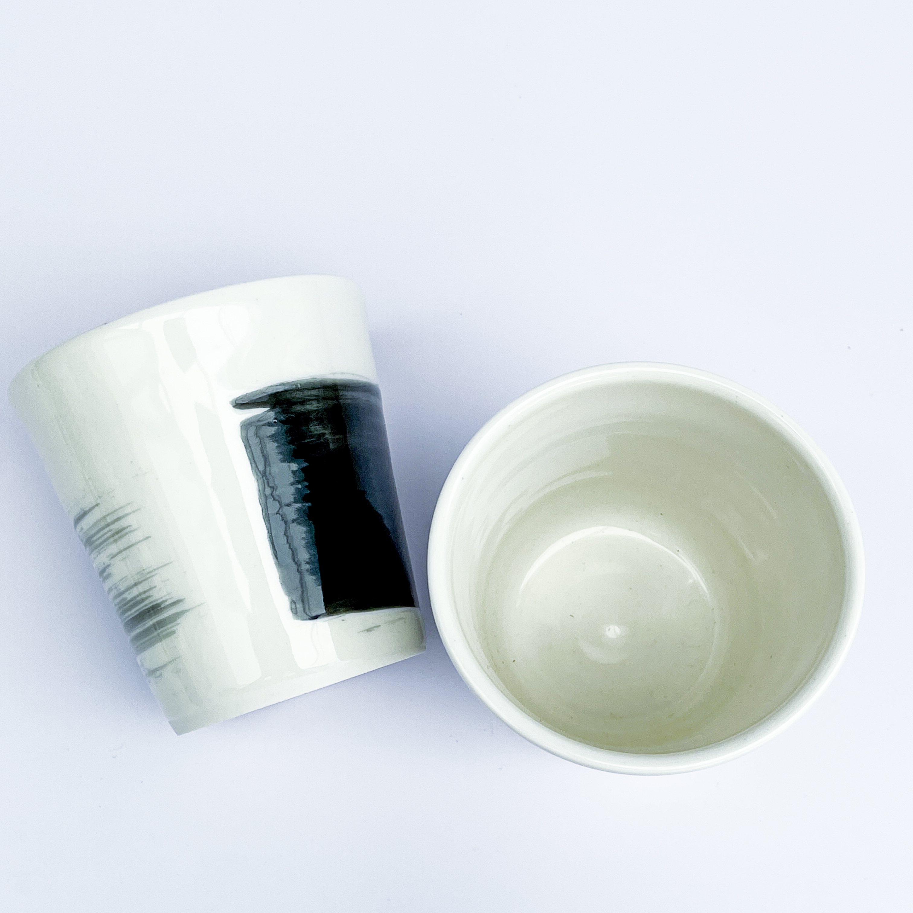 Two porcelain tumblers with black abstract decoration from above, one is lying on it's side
