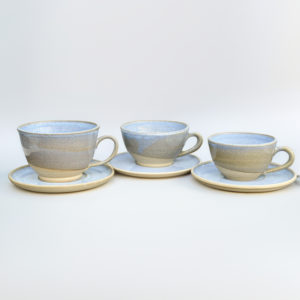 Three cappuccino cup and saucer sets ranging in size from large to small, glazed in speckled pale blue with bare clay bottoms
