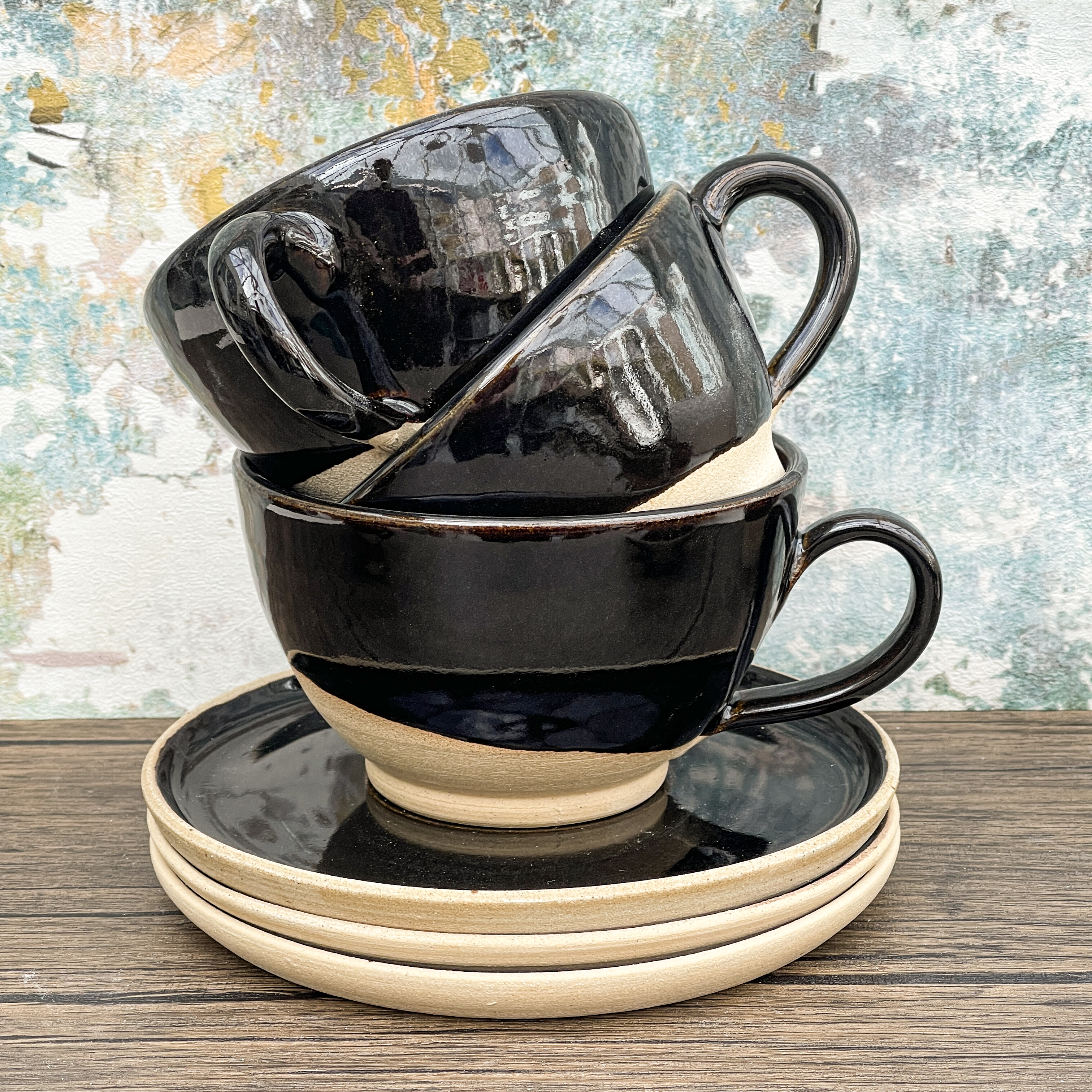 Three half glazed black cappuccino cups stacked inside each other on a wooden table